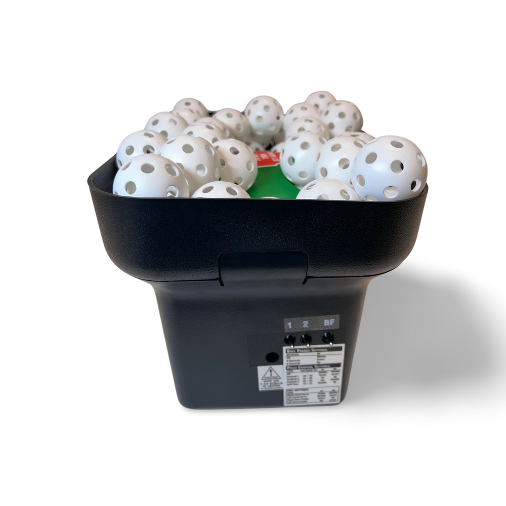 Pitching machine from the left, hopper full of white balls and the switch panel on the side